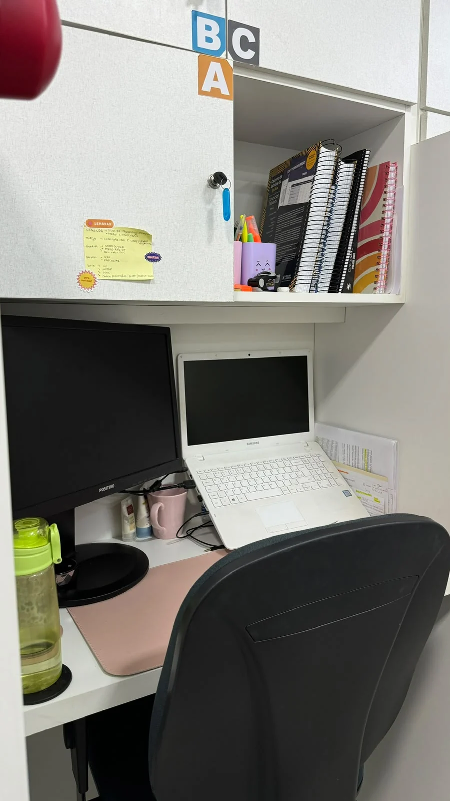 Mesa de cabine organizada com notebook, monitor e materiais de estudo